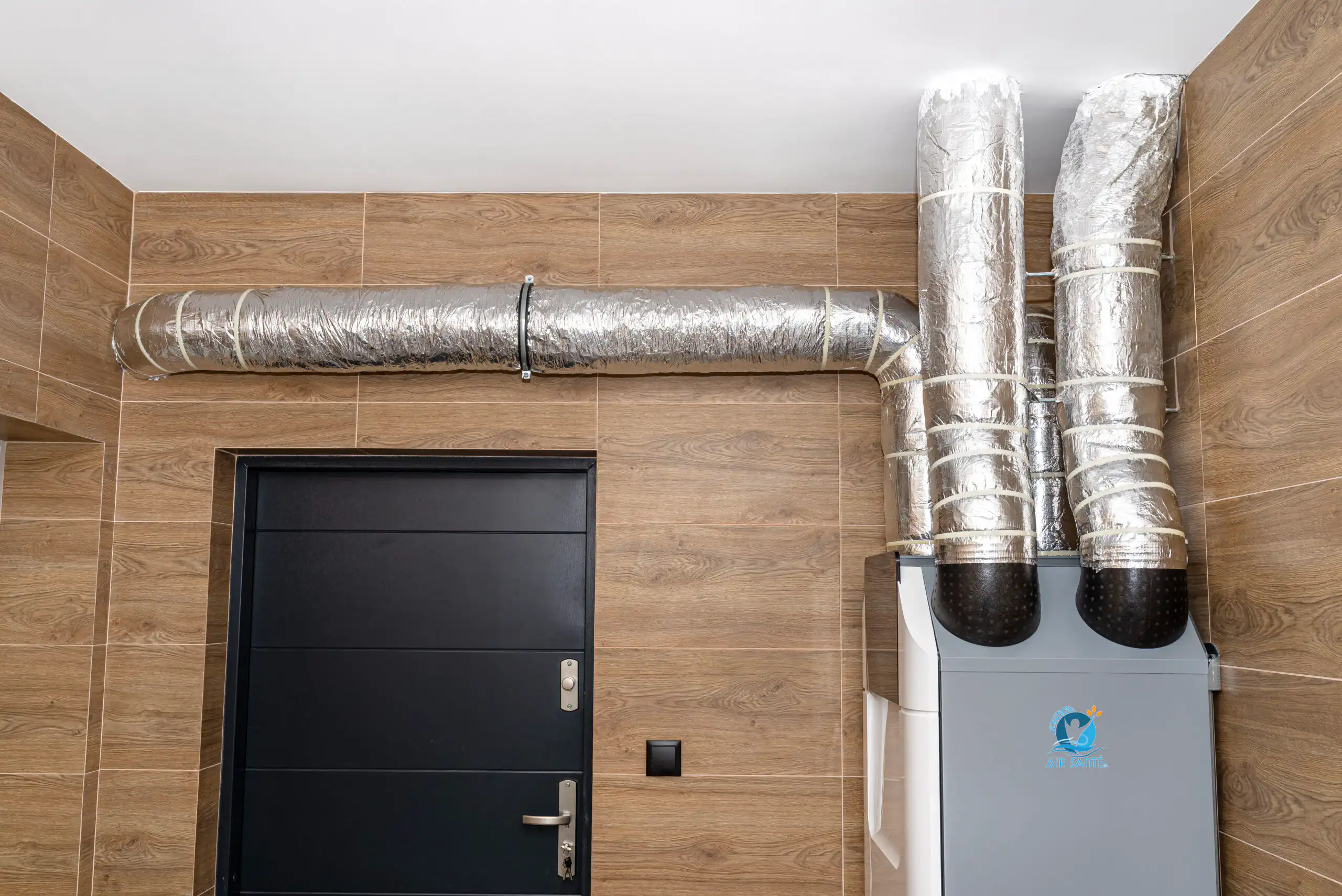 Home mechanical ventilation with heat recovery hanging on the wall in a modern gas boiler room with brown ceramic tiles imitating wood.